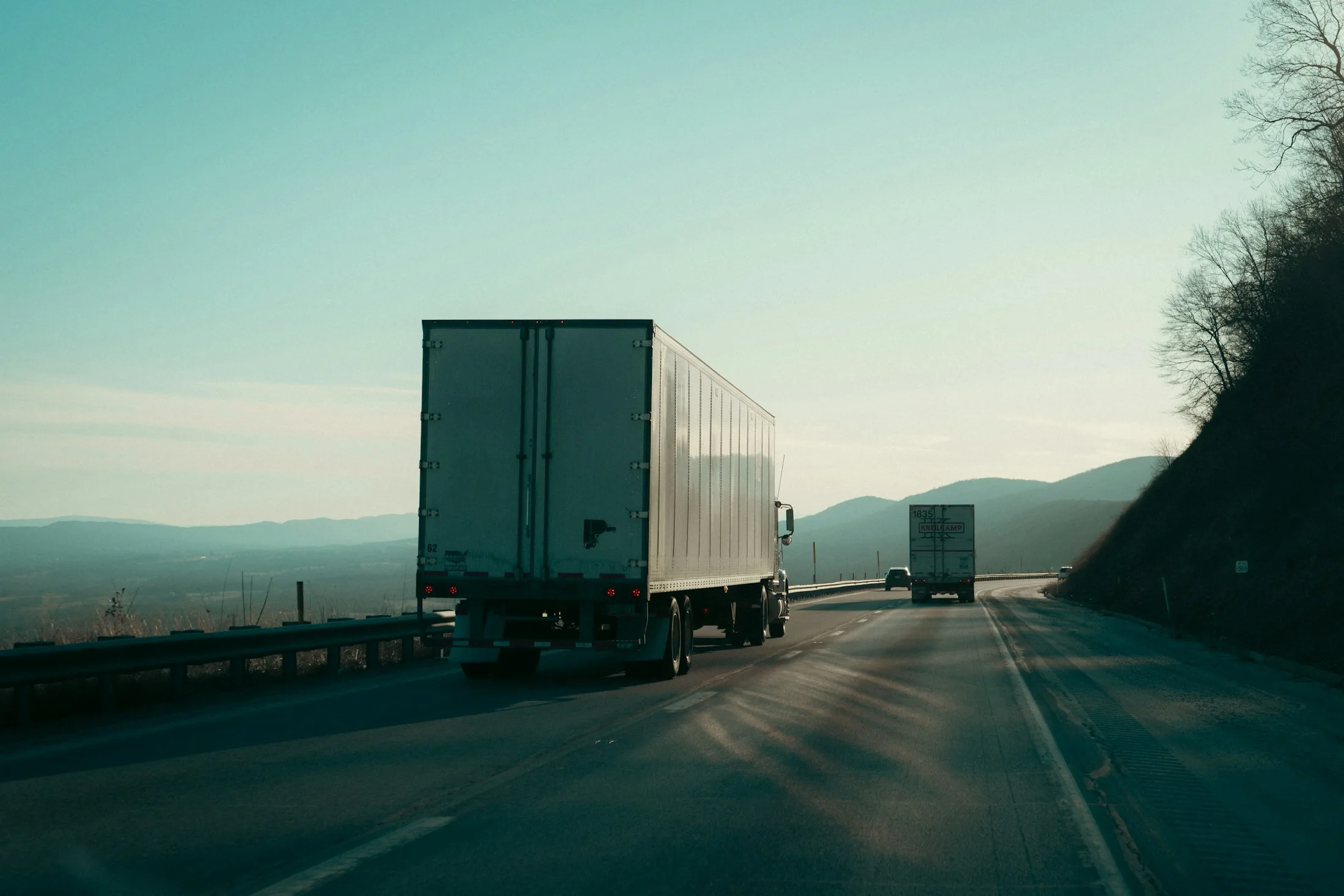 Semi-trucks traveling along a scenic U.S. highway through the mountains